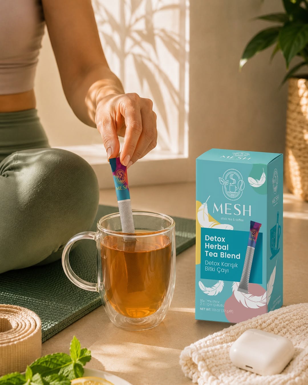 Cam fincandaki çayı Mesh Stick'le karıştıran el, yanında Detox kutusu